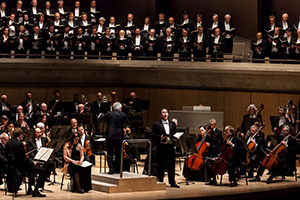 Photo of TMC performing with the TSO at Roy Thomson Hall. The orchestra and soloists are on stage and the Choir is in the choir loft. Peter Oundjian is on the podium conducting.